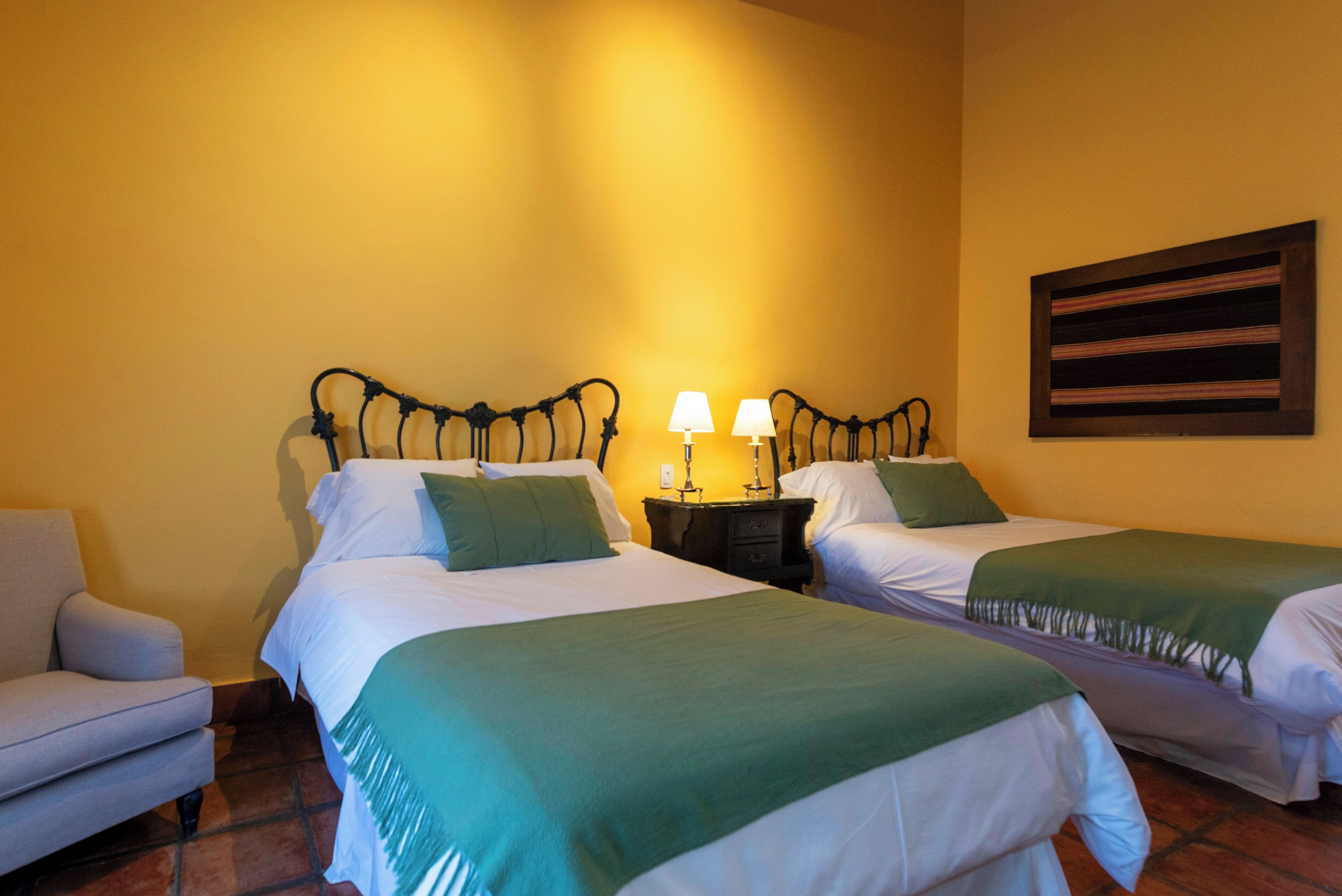 A hotel room with two beds, a nightstand with lamps, a chair, and a wall painting.