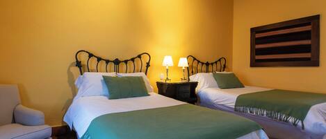 Une chambre d’hôtel avec deux lits, une table de chevet avec des lampes, une chaise et un tableau au mur.