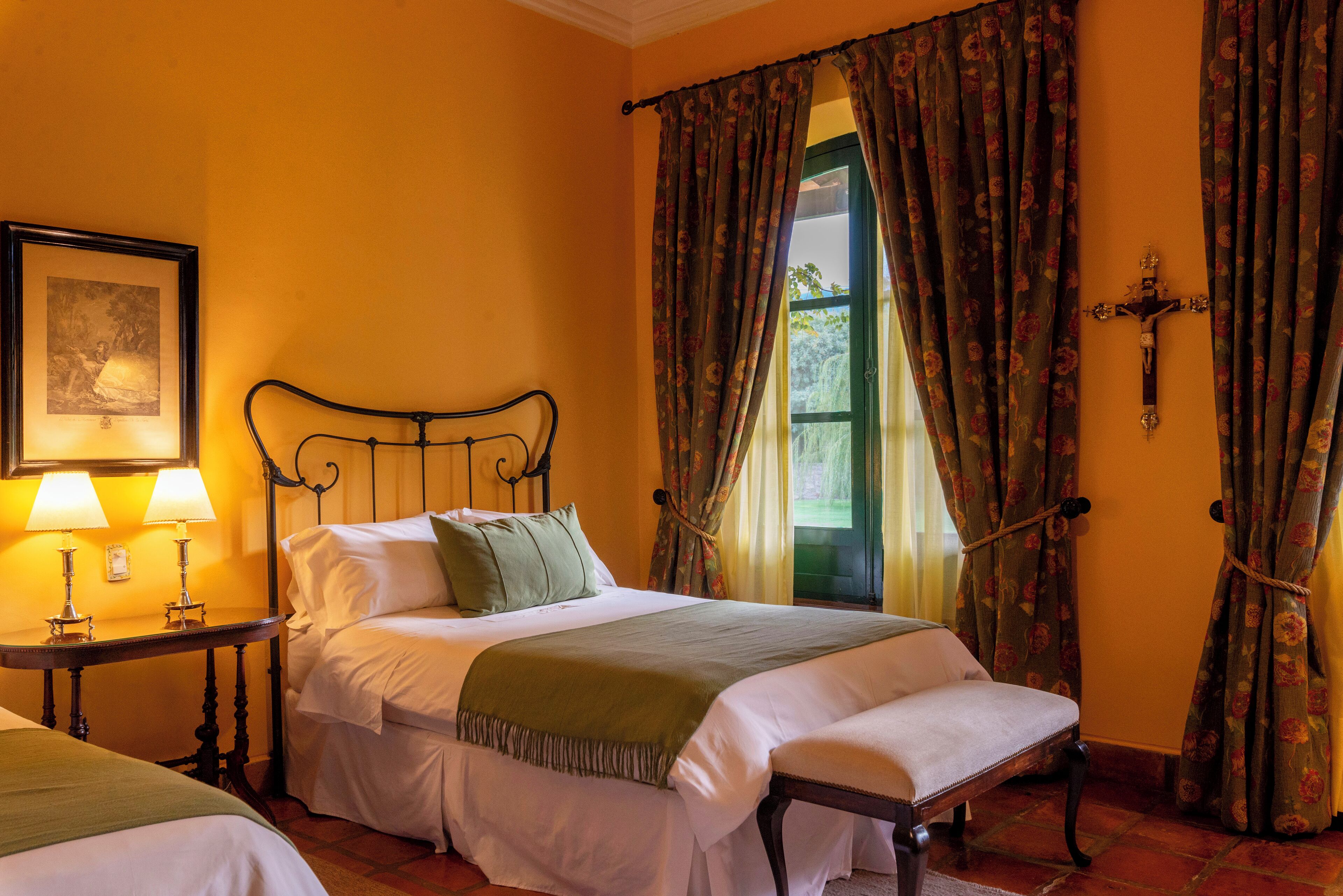 Un dormitorio con cama, mesitas de noche y una ventana con cortinas florales.