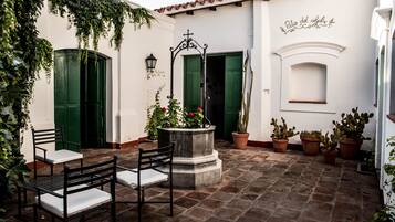 A courtyard with a stone floor, green doors, and potted plants.