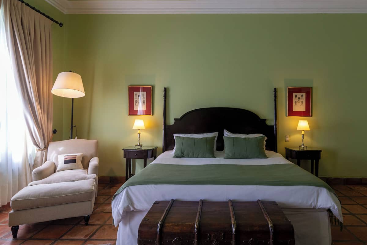 A hotel room with a bed, a chair, two bedside tables with lamps, and two framed pictures on the walls.
