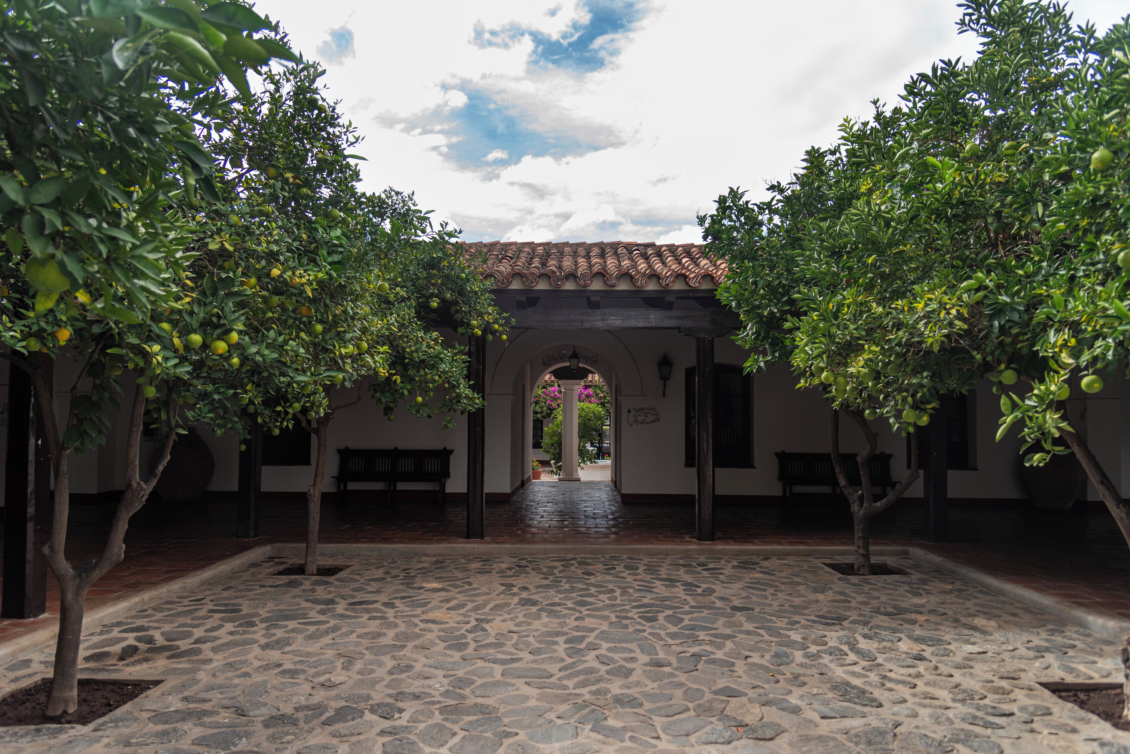 A courtyard with a stone floor, trees with fruit, and a tiled roof.
