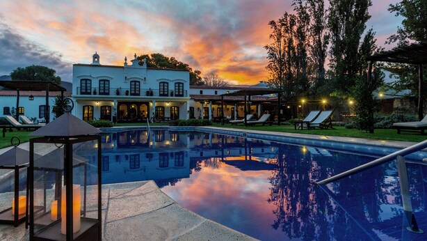 Una piscina con sillas de descanso y un pabellón, rodeada por un edificio con varias ventanas y balcones.