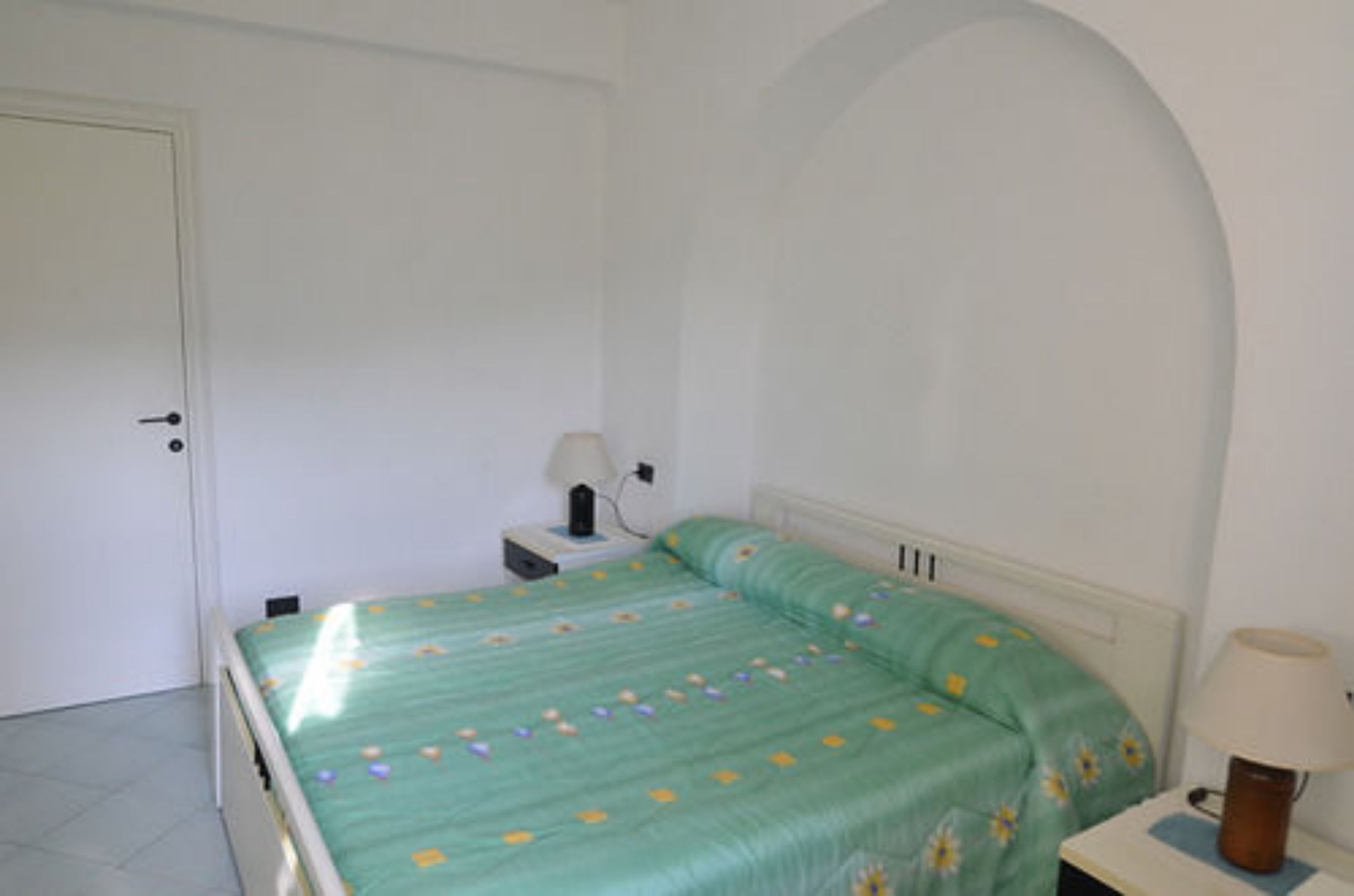 A simple, clean room with a bed, a nightstand, and a lamp.