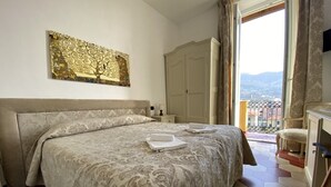 A hotel room with a large bed, a nightstand, a wardrobe, and a view of the city through a balcony.
