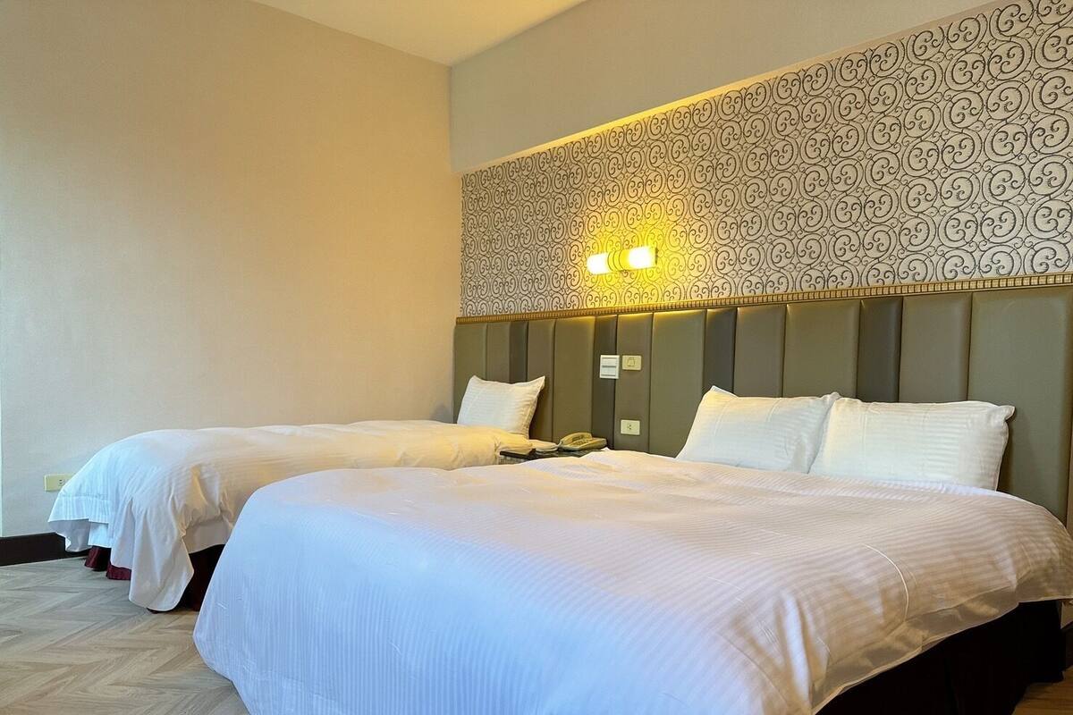 A hotel room with two beds, a patterned headboard, and a wall-mounted light fixture.