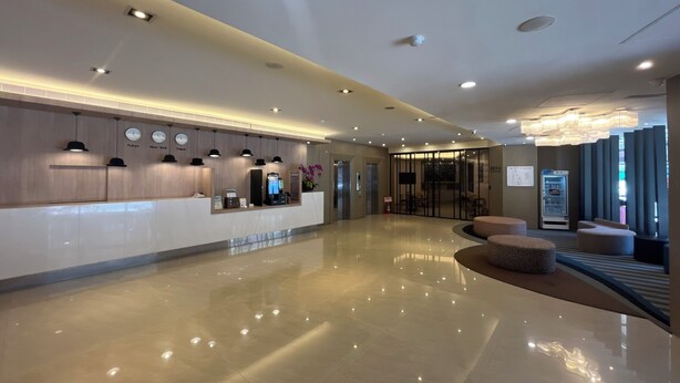 Un hall d’hôtel moderne avec un comptoir d’accueil, une horloge numérique et un espace salon.