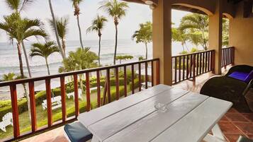 A covered outdoor area with a white table and chairs, a view of the ocean, and palm trees.
