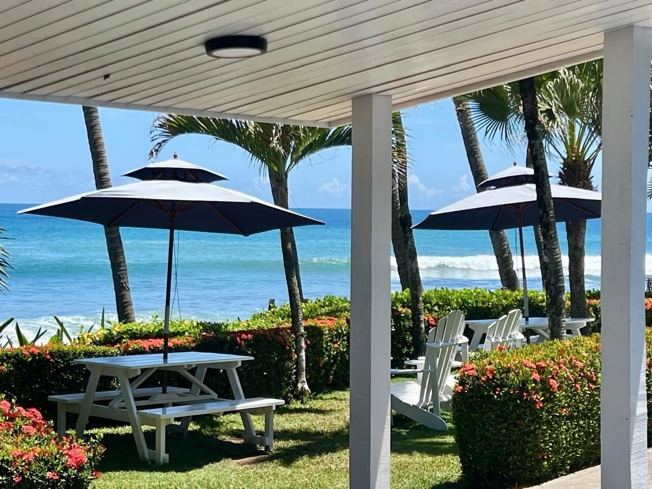 An outdoor seating area with tables and chairs, umbrellas, and a view of the ocean.