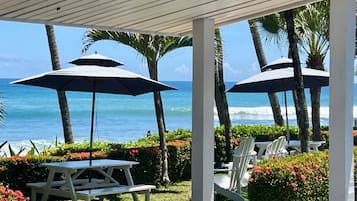 An outdoor seating area with tables and chairs, umbrellas, and a view of the ocean.