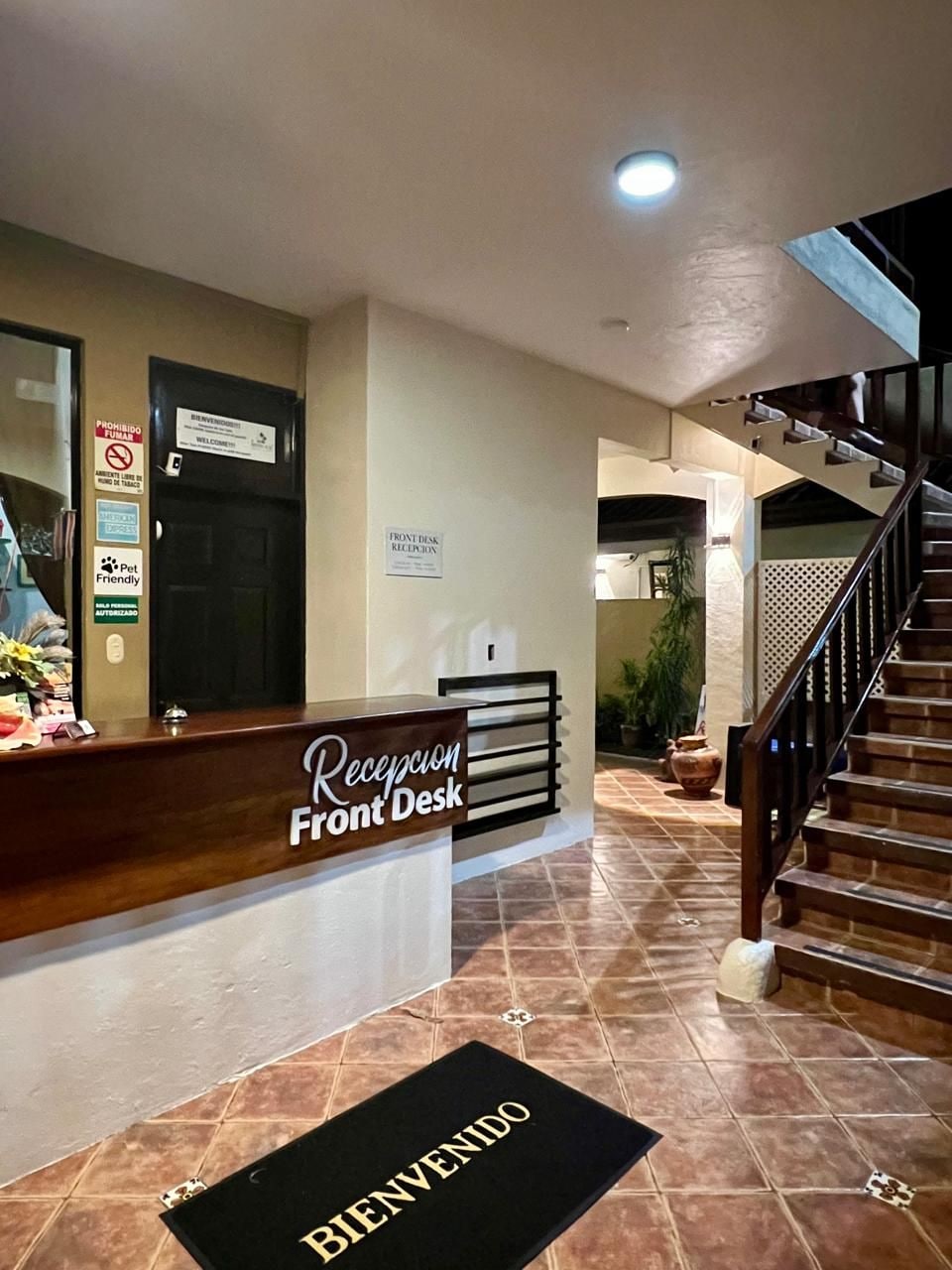 A hotel reception desk with a 'Welcome' mat, a staircase, and a 'Front Desk' sign.