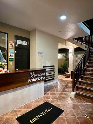 A hotel reception desk with a 'Welcome' mat, a staircase, and a 'Front Desk' sign.