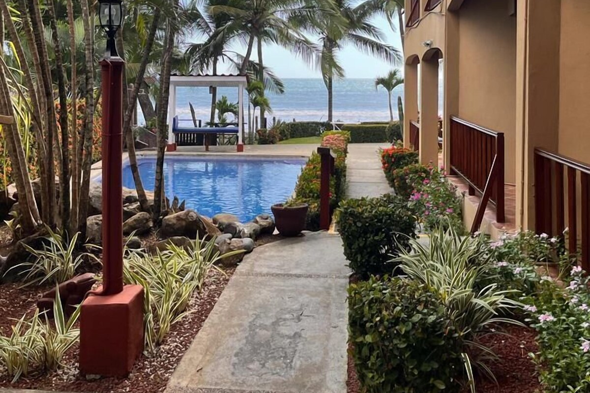 A pool area with a pathway, palm trees, and a view of the ocean.