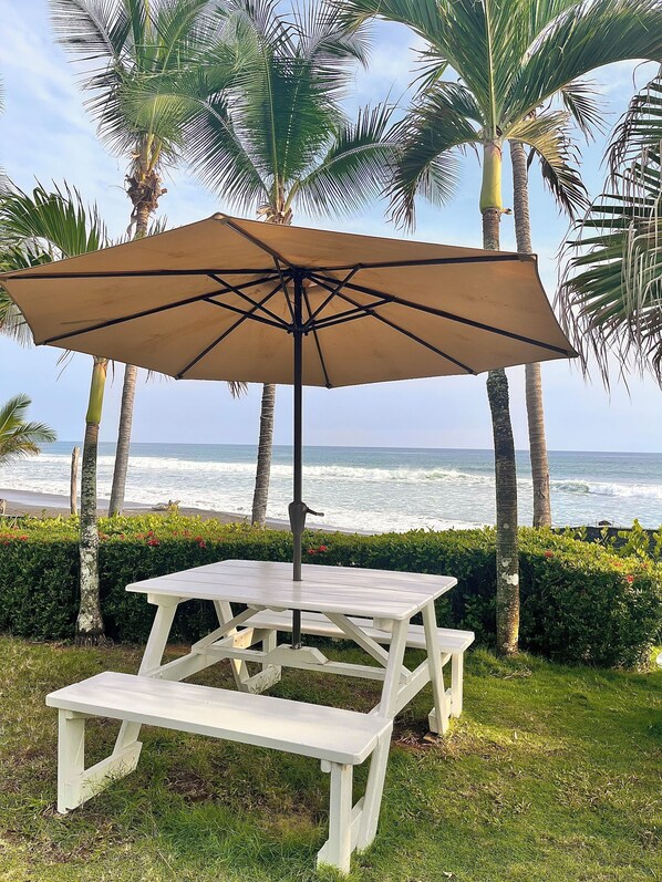 A picnic table with a canopy, surrounded by palm trees and a view of the ocean. - The Backyard Hotel (Jacó)