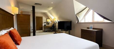 A hotel room with a large bed, a desk, a television, and a window.