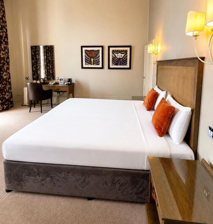 A hotel room with a large bed, a desk with a chair, and two framed artworks on the wall.