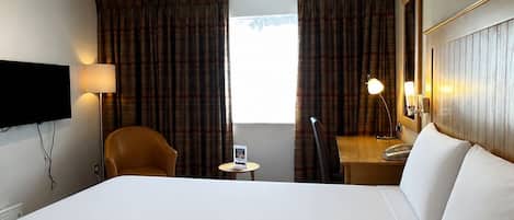 A hotel room with a large bed, a desk with a lamp, a chair, and a television mounted on the wall.