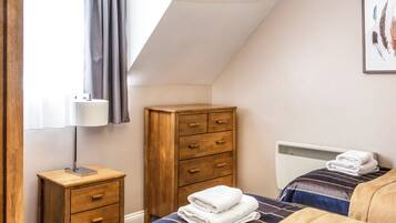 Quarto com cama, cómoda de madeira, radiador e janela com cortinas.