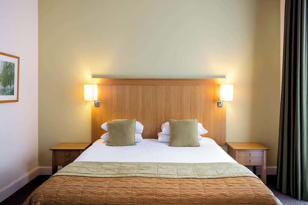 Hotellihuone, jossa on suuri sänky, kaksi yöpöytää ja sängynpääty, jossa on seinään kiinnitetyt valaisimet.