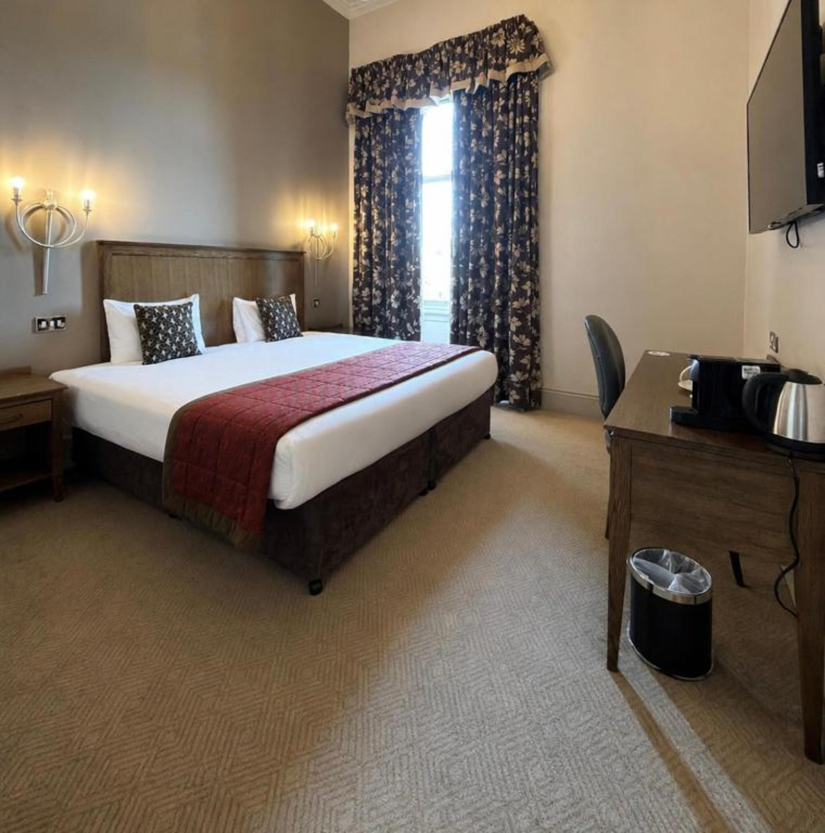 Une chambre d’hôtel avec un grand lit, un bureau, une chaise, une poubelle et un téléviseur.