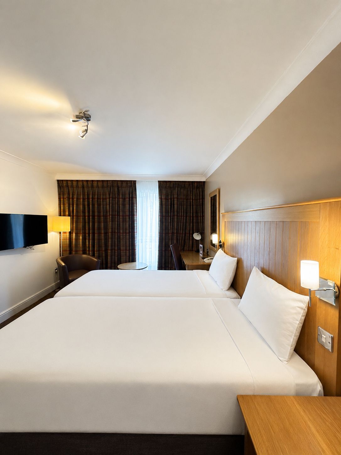 Quarto de hotel com duas camas, televisão, escrivaninha e cadeira.