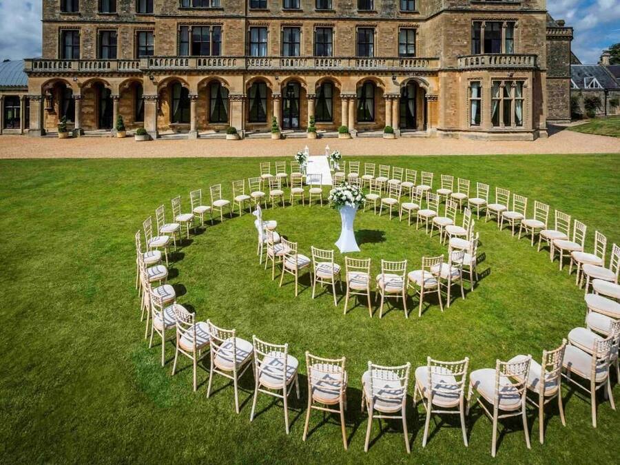 A circular outdoor seating arrangement with chairs and a central floral arrangement, set against a historic building facade.