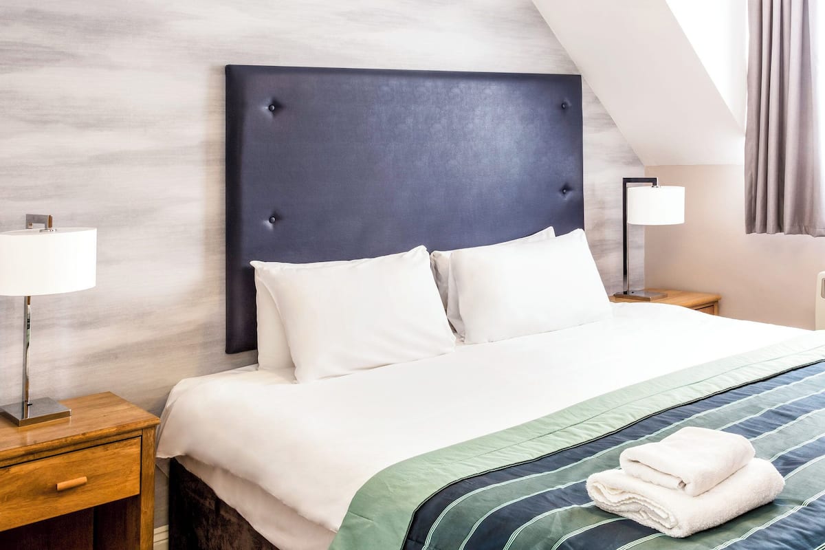 Hotellihuone, jossa on suuri sänky, kaksi yöpöytää, lamppu ja näkymä taivaalle.