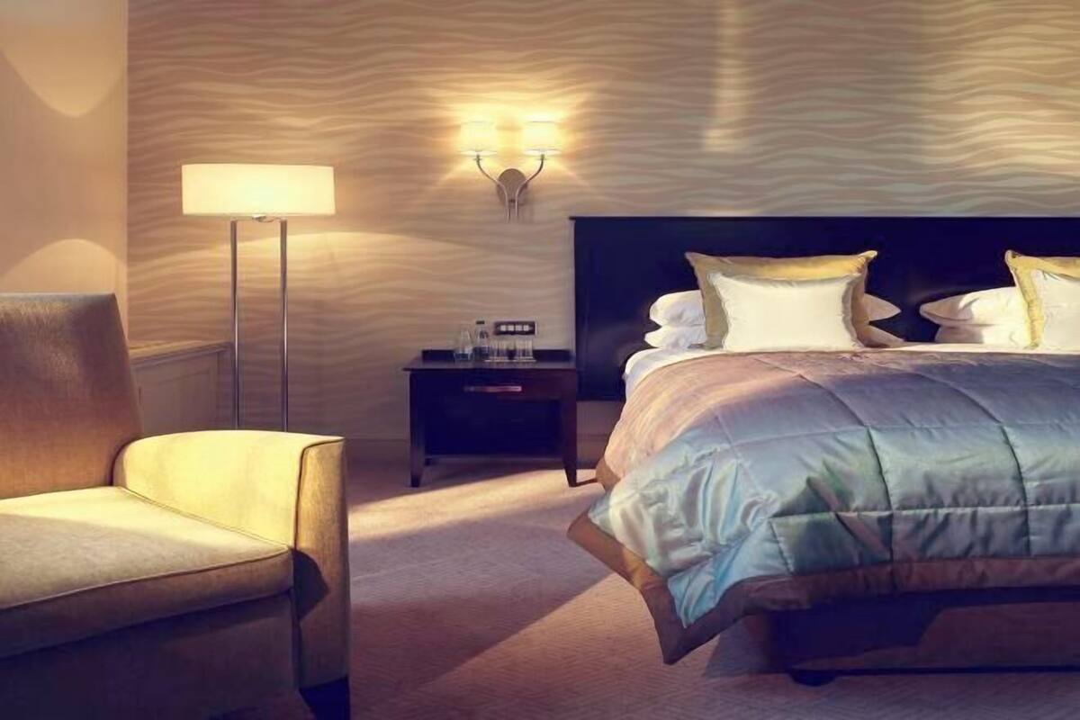 Hotellihuone, jossa on sänky, tuoli, yöpöytä ja lamppu.