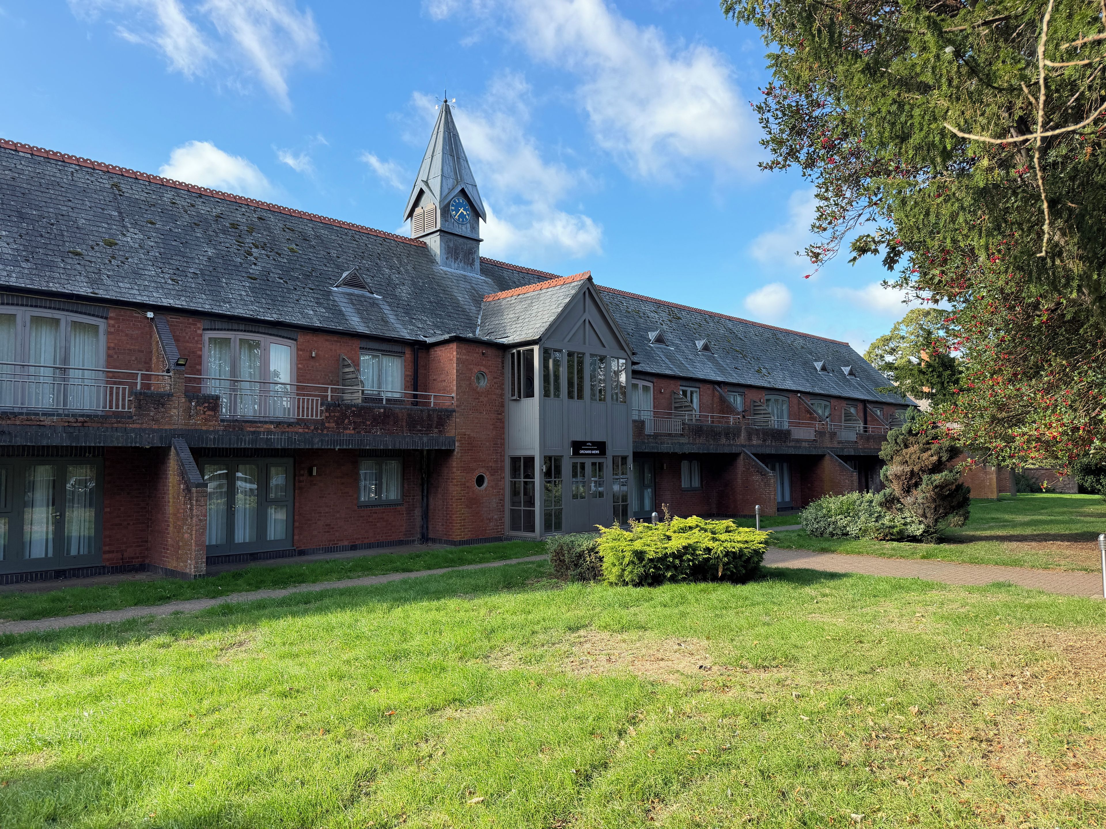A building with multiple windows, a clock tower, and a well-maintained lawn.