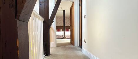 A hallway with a herringbone carpet, wooden beams, and a white door leading to a bedroom.