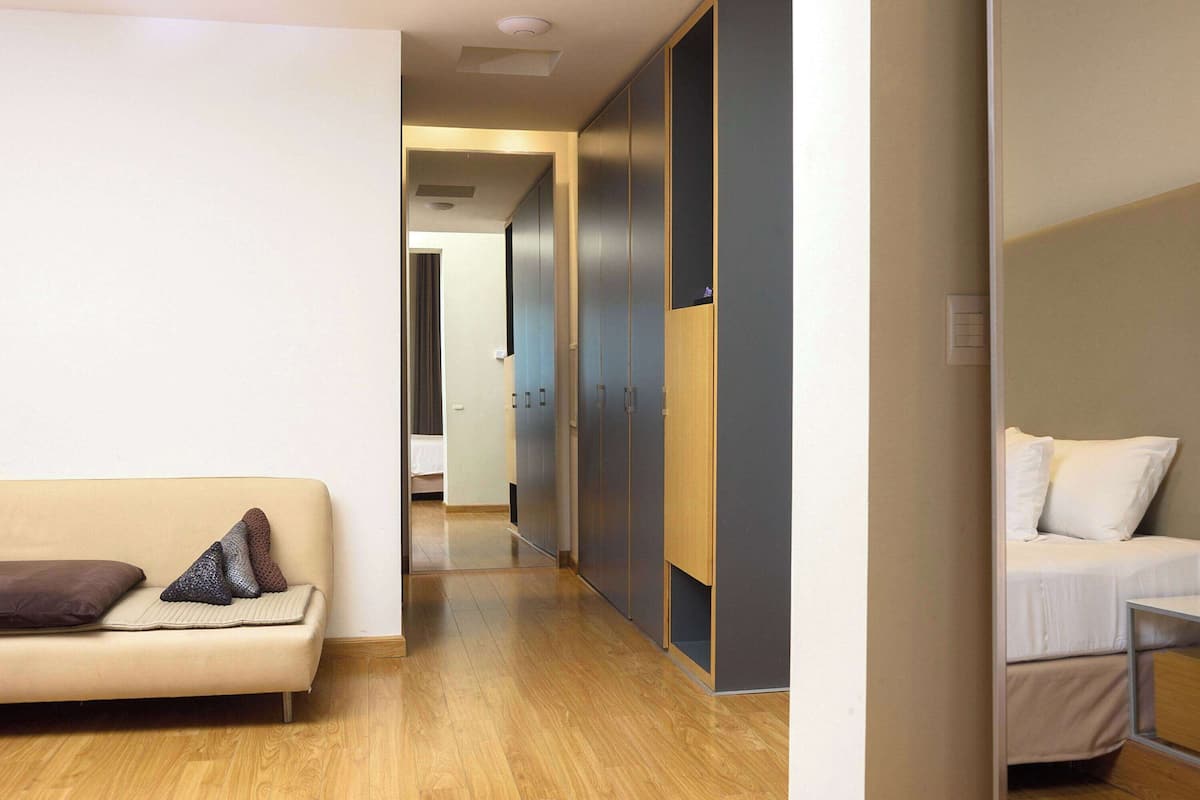 Une chambre d’hôtel avec un plancher en bois, un canapé avec des coussins, un lit avec une literie blanche et une armoire avec des portes coulissantes.