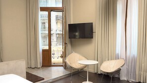Een hotelkamer met balkon, een aan de muur bevestigde televisie en twee stoelen met een tafeltje.