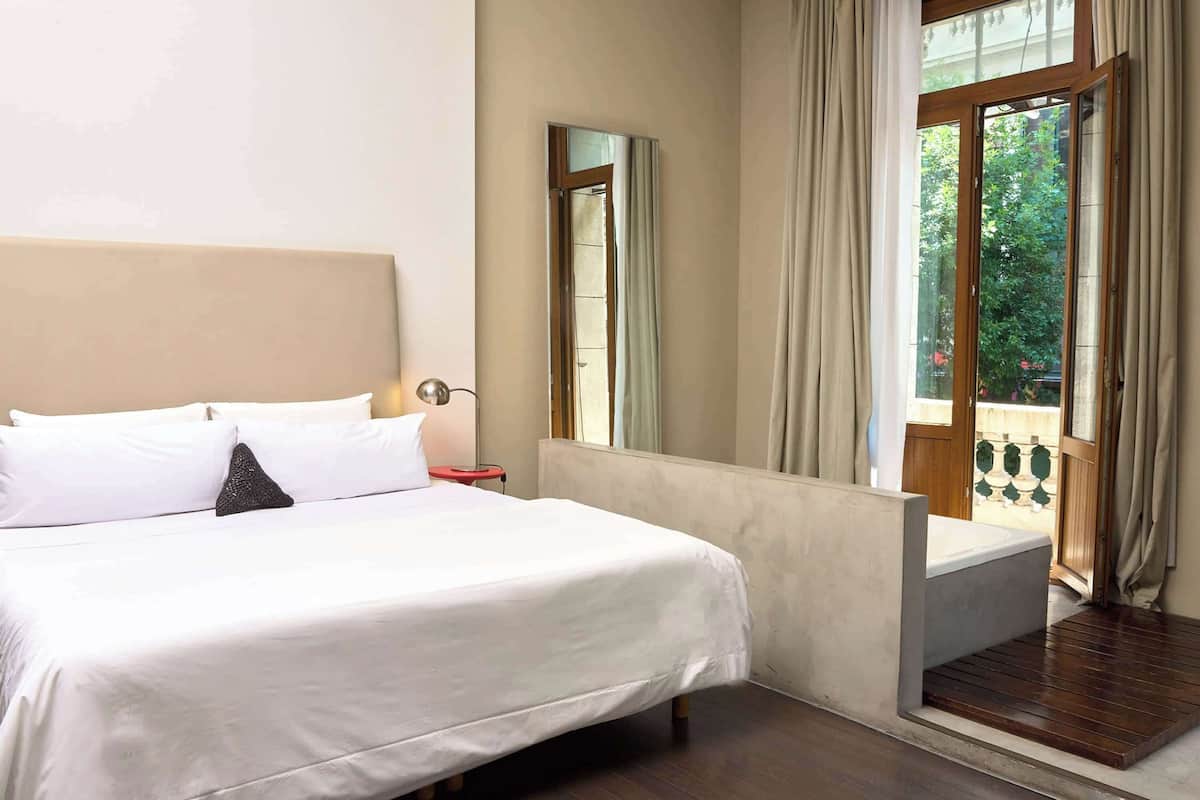 Une chambre d’hôtel avec un grand lit, une table de chevet, un miroir et une vue sur l’extérieur par une porte.