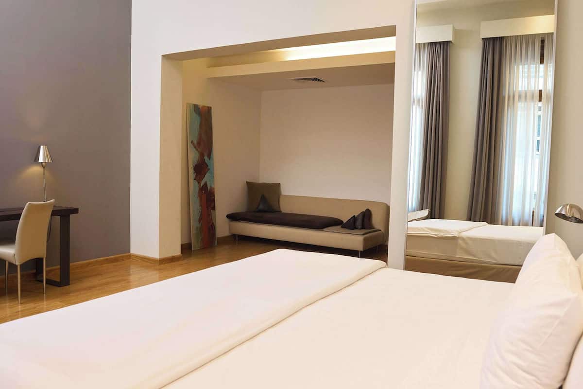 Une chambre d’hôtel avec un lit, un bureau, une chaise, un canapé et un grand miroir.