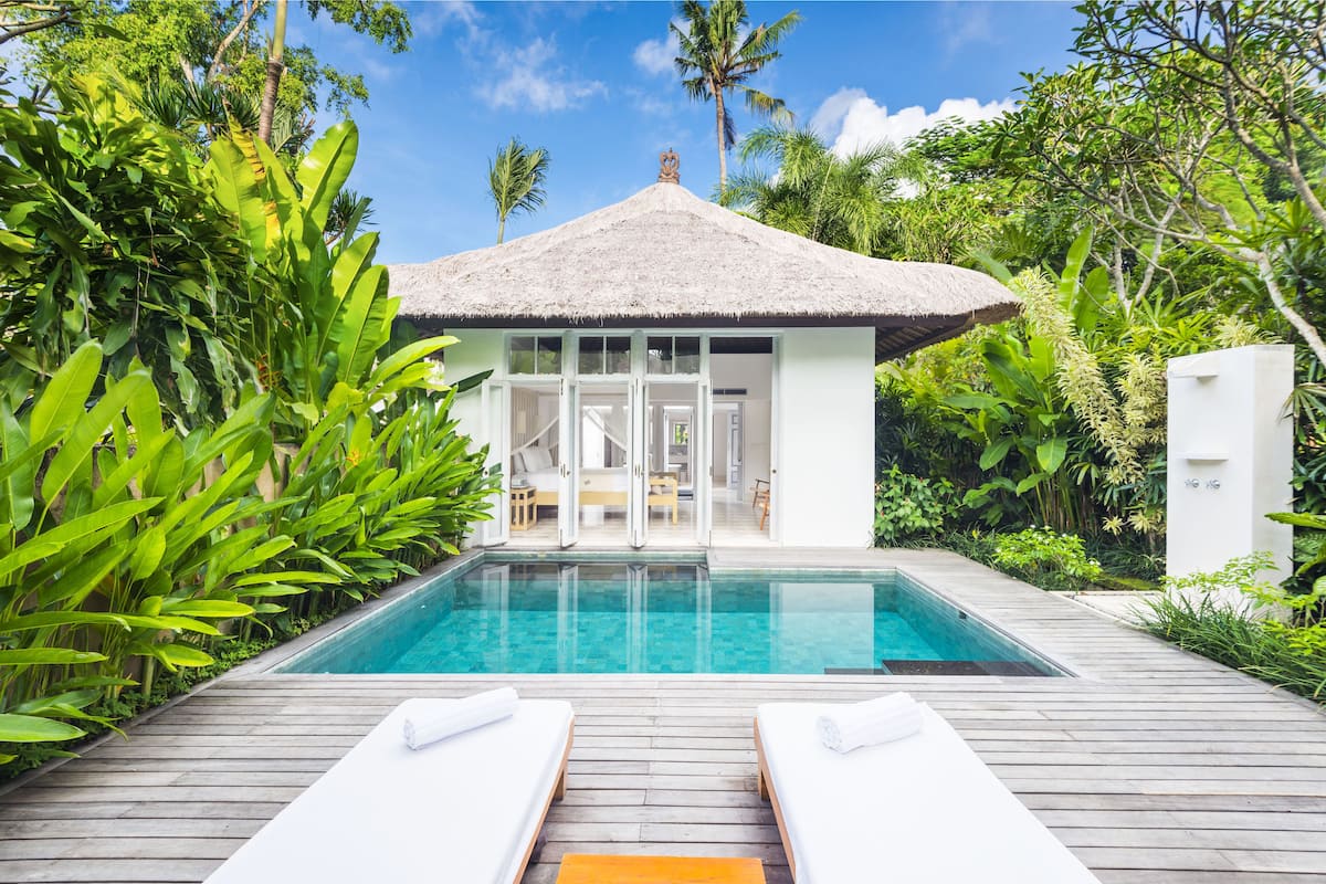A poolside area with a thatched-roof structure, surrounded by lush greenery.