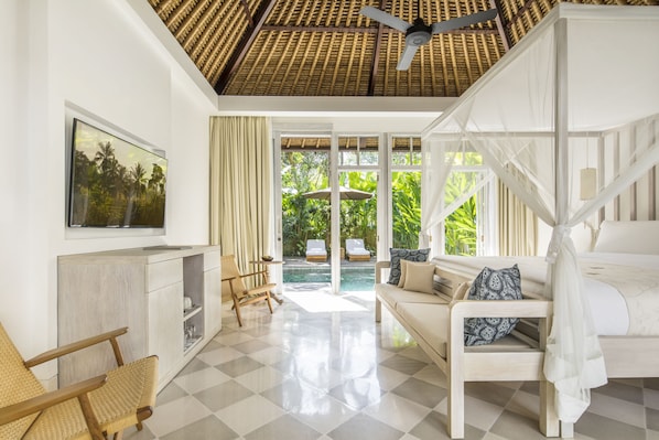 A spacious room with a checkered floor, a bed with a canopy, a TV mounted on the wall, and a view of an outdoor pool area. - COMO Uma Ubud (Ubud)