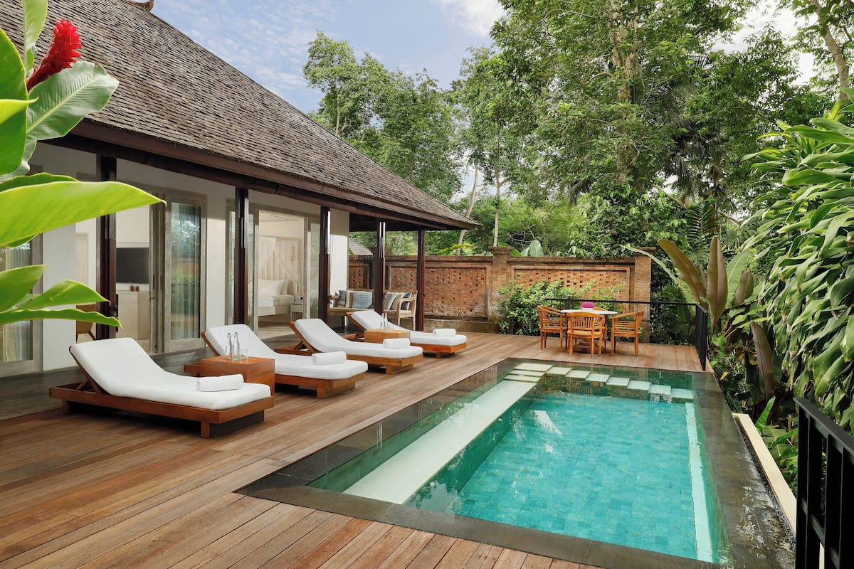A poolside area with wooden deck, lounge chairs, and a brick wall.