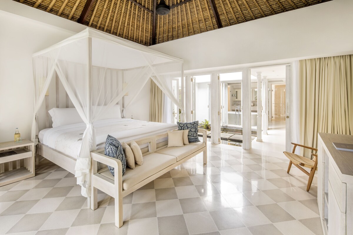 A spacious bedroom with a four-poster bed, a bench, and a daybed.