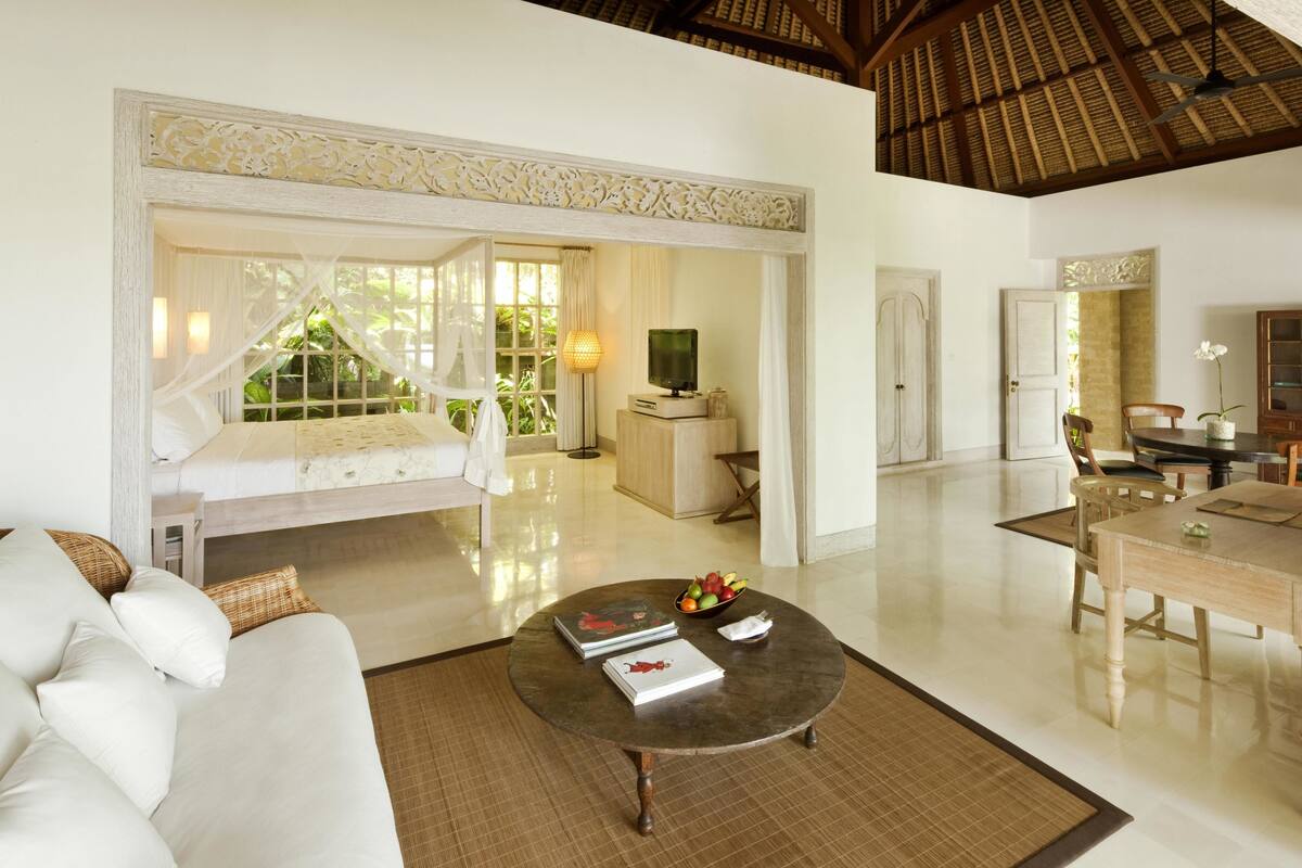 A spacious living area with a sofa, a coffee table with books and fruit, a TV, and a dining table with chairs.