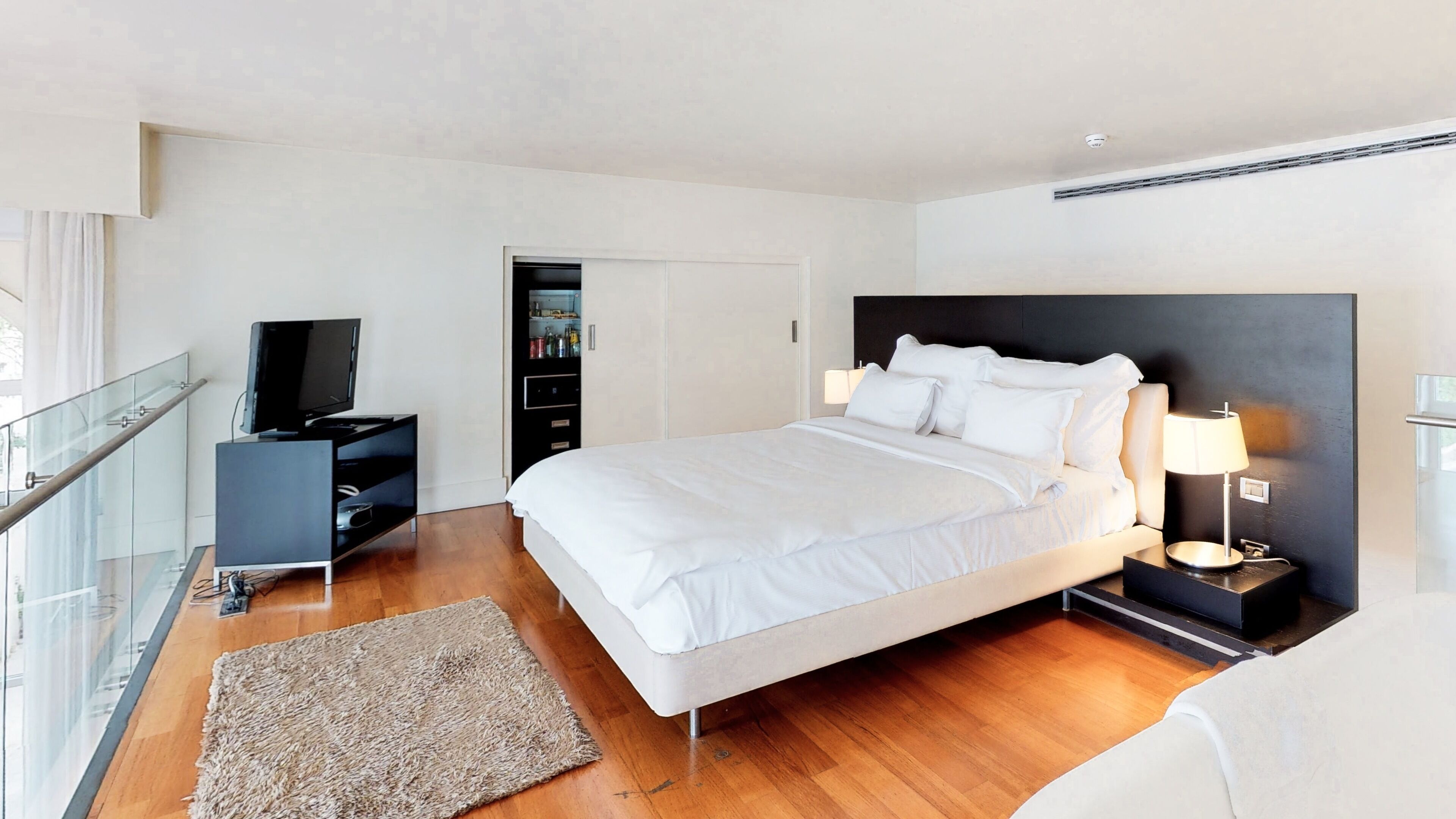 Una habitación de hotel moderna con una cama grande, televisión, armario y balcón.