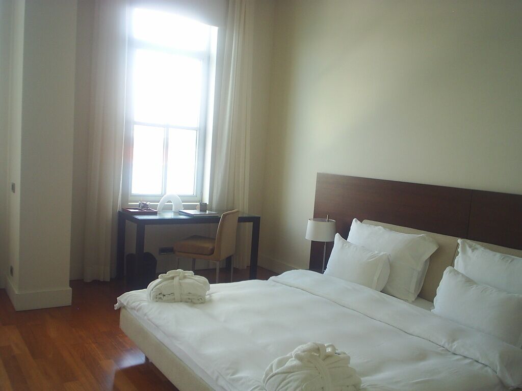 A hotel room with a bed, a desk, a chair, and a lamp.