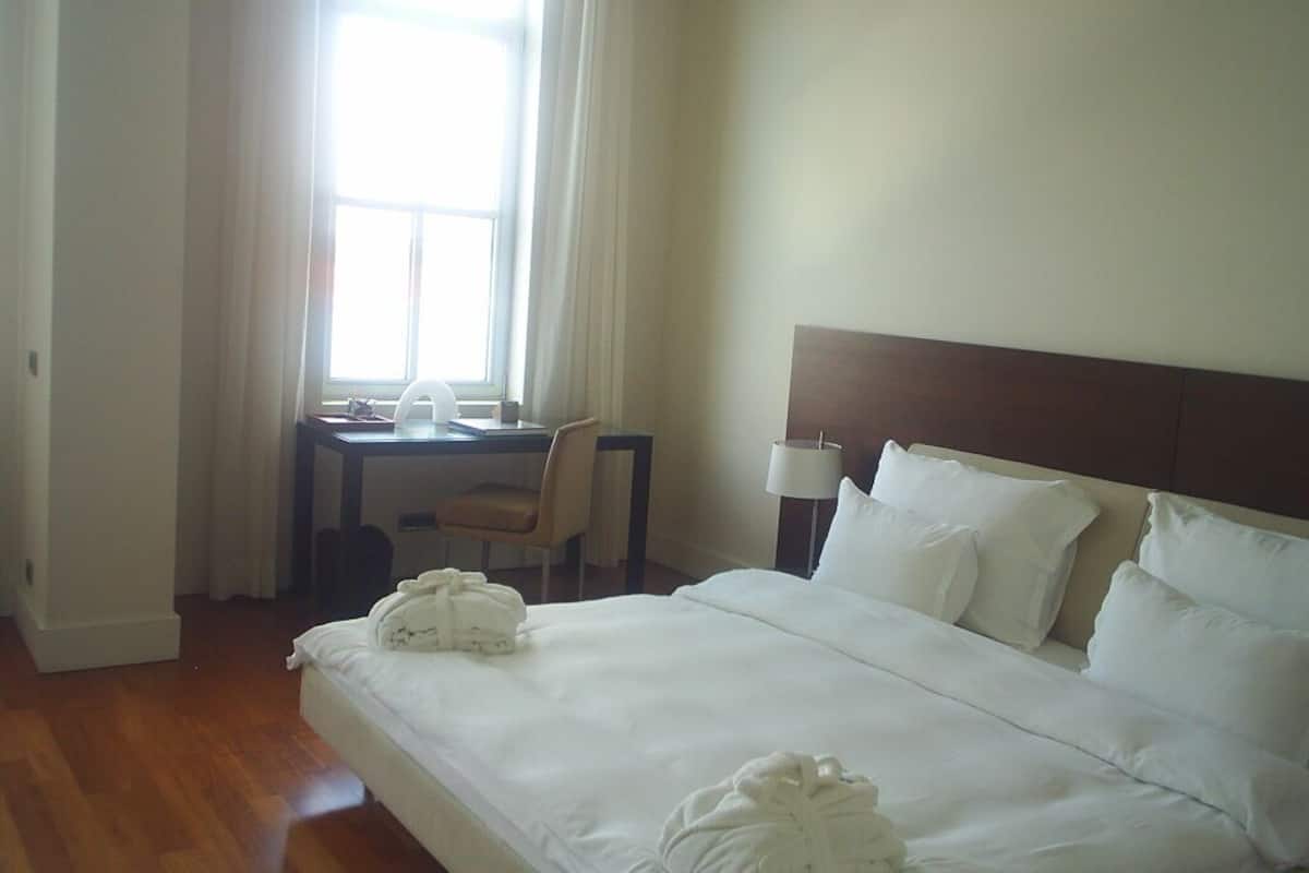 A hotel room with a bed, a desk, a chair, and a lamp.