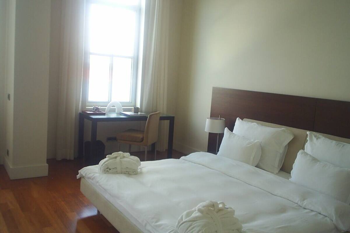 A hotel room with a bed, a desk, a chair, and a lamp.