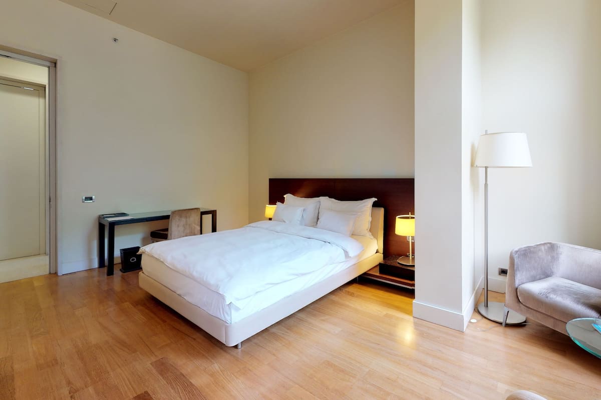 A hotel room with a large bed, a desk, a chair, and a floor lamp.