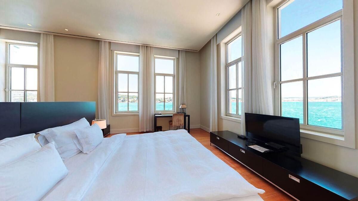 Una cama grande con ropa blanca, un televisor de pantalla plana y vistas al mar a través de amplias ventanas.
