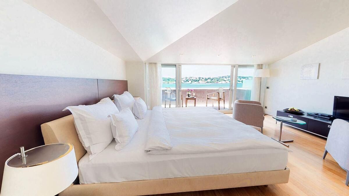 Ein modernes Hotelzimmer mit einem großen Bett, einem Balkon mit Aussicht, einem Schreibtisch mit Fernseher und einer Lampe.