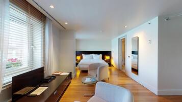 A modern hotel room with a large bed, bedside lamps, a glass coffee table, and a seating area with a sofa.