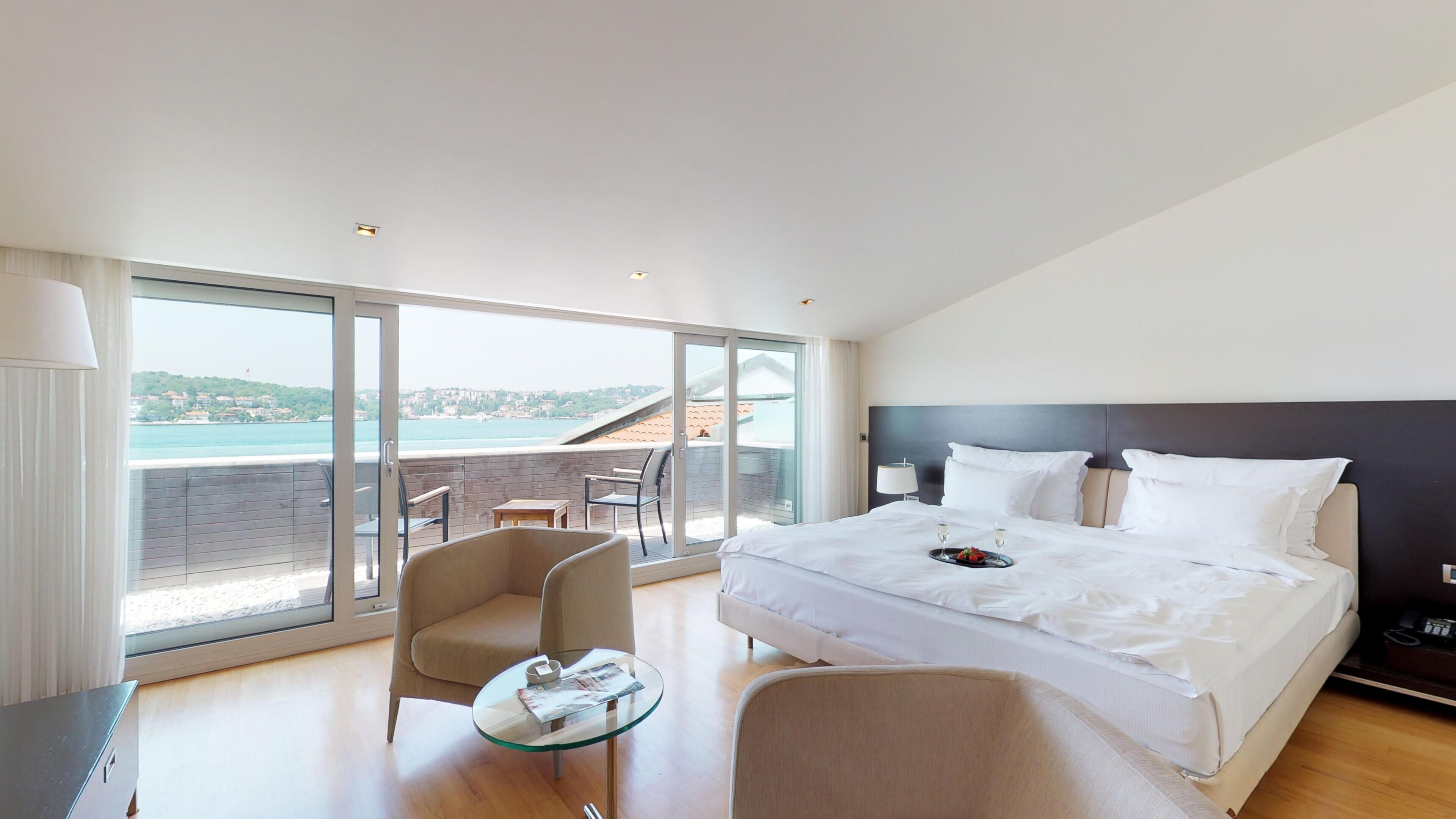 Habitación de hotel moderna con una cama grande, una mesa de vidrio, una silla y vistas al mar.