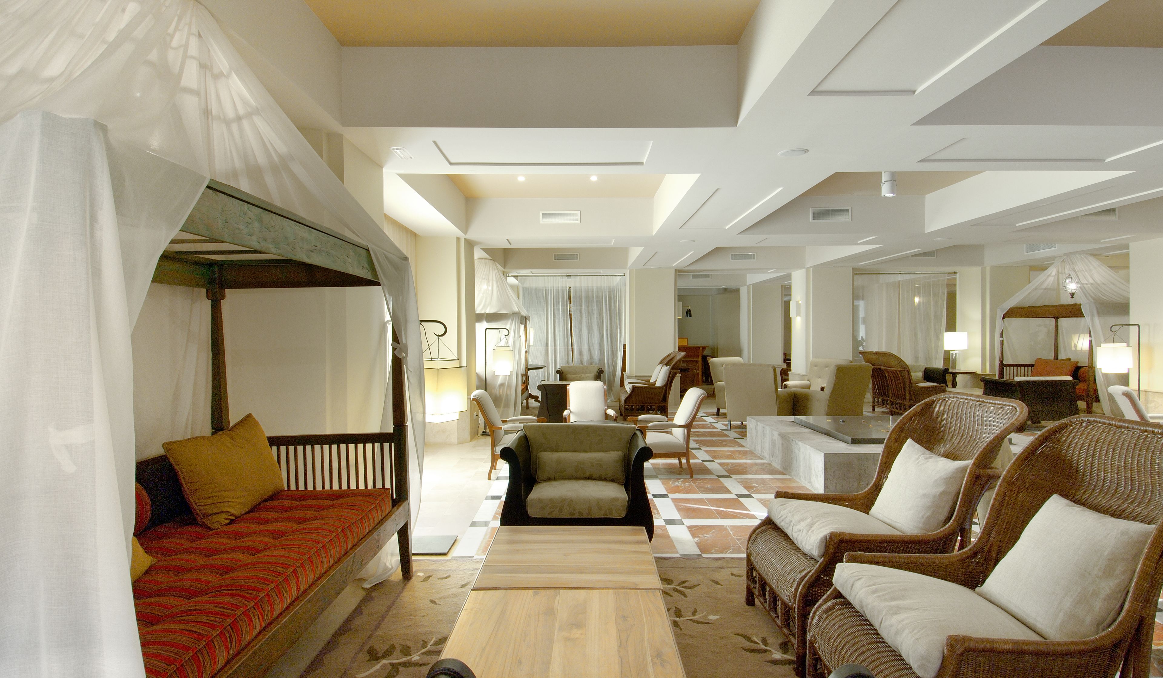 Un hall d’hôtel spacieux avec un sol à carreaux, plusieurs coins salon comprenant un canapé et des fauteuils, et un lit à baldaquin.