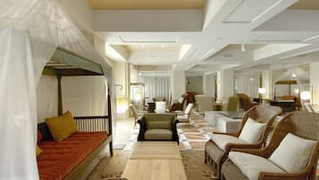 Un hall d’hôtel spacieux avec un sol à carreaux, plusieurs coins salon comprenant un canapé et des fauteuils, et un lit à baldaquin.